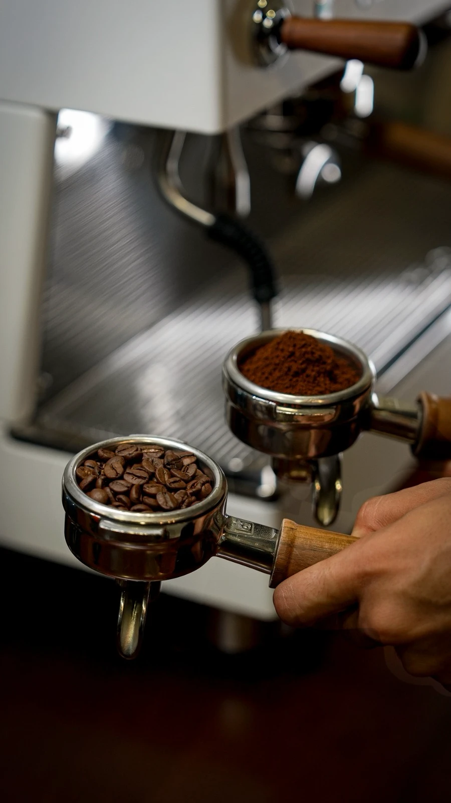 Café en grano y molido en portafiltros junto a una máquina de espresso